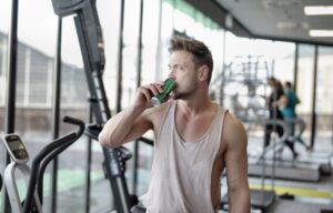 Tired young male athlete drinking energy drink while resting after workout in gym